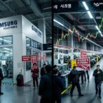 A dramatic split screen showing Samsung Electronics semiconductor factory and Hyundai Motor assembly line both affected by red strike warning signs and picketing workers, with KOSPI index chart showing volatility in the background, realistic modern Korean industrial setting, cinematic lighting