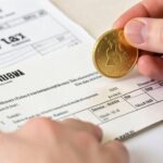 A large dividend check with a gold coin falling into a hand, and tax forms in the background showing a downward arrow for tax.