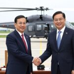 A symbolic handshake between South Korean and Bangladeshi officials with LH Mi-ru helicopters in the background, representing defense export diplomacy in 2026, professional business meeting atmosphere